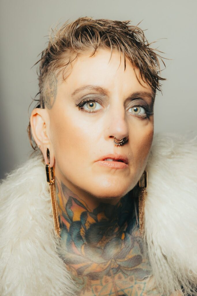 Studio brand portrait of Chari playing her custom washboard-and-cymbal percussion rig, eyes lowered in concentration against a warm gray backdrop, Ashland Oregon musician branding photography.