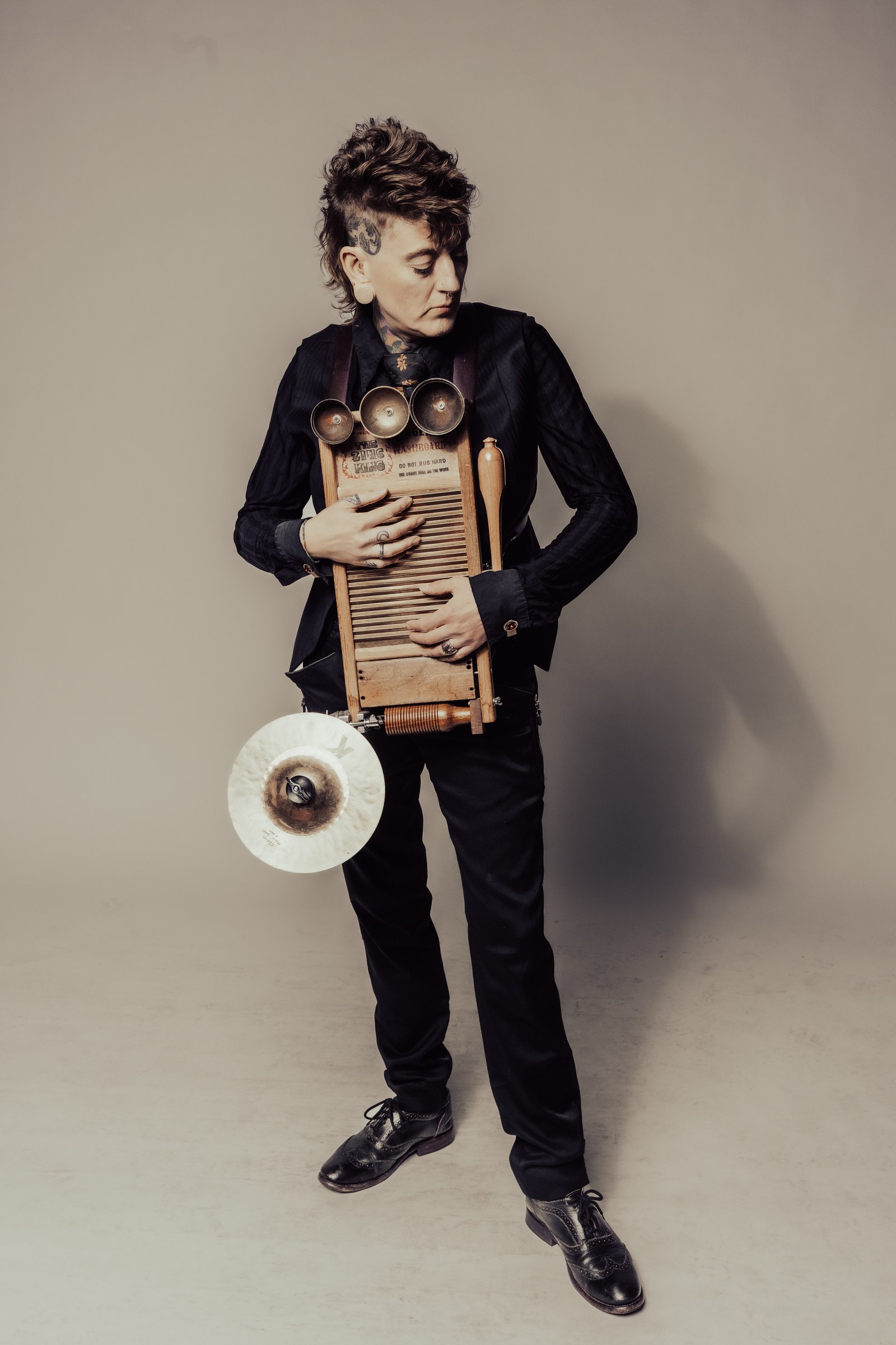 Chari holding her washboard instrument in a tailored black suit