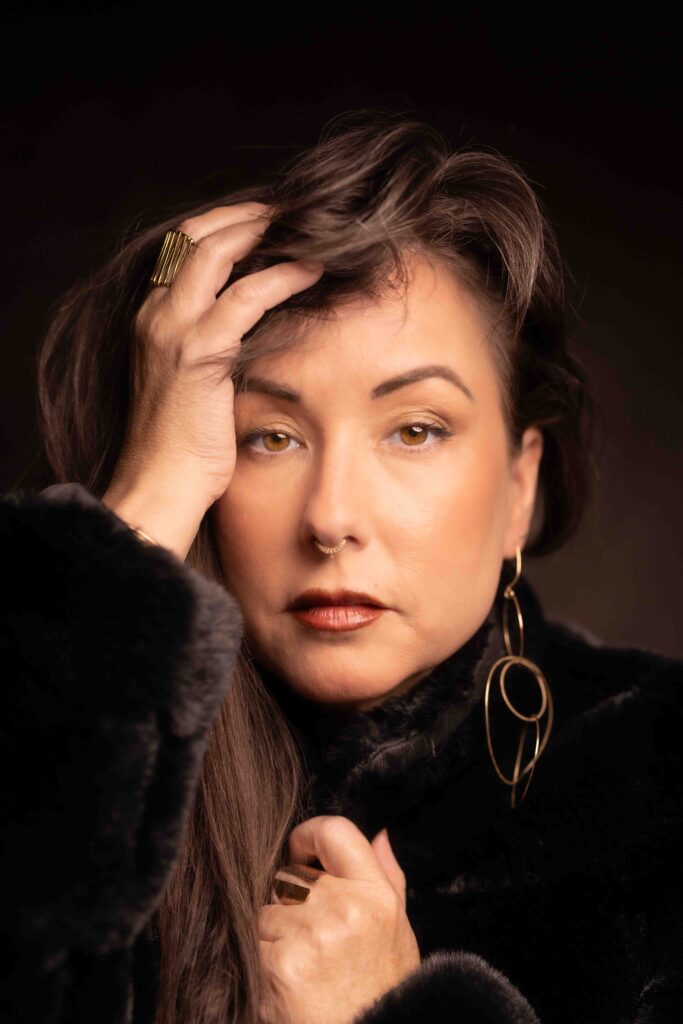 Portrait of Napili Sharma in a black coat against a black studio backdrop, Ashland Oregon